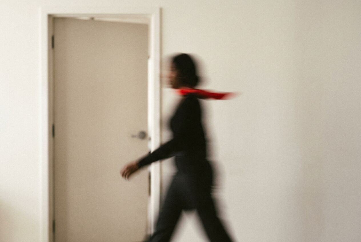 A blurred figure in black with a red scarf walking quickly past an open door